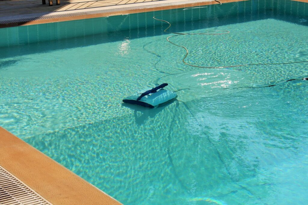 Poolroboter am Beckenboden, sein Kabel schwimmt in Bögen auf dem Wasser