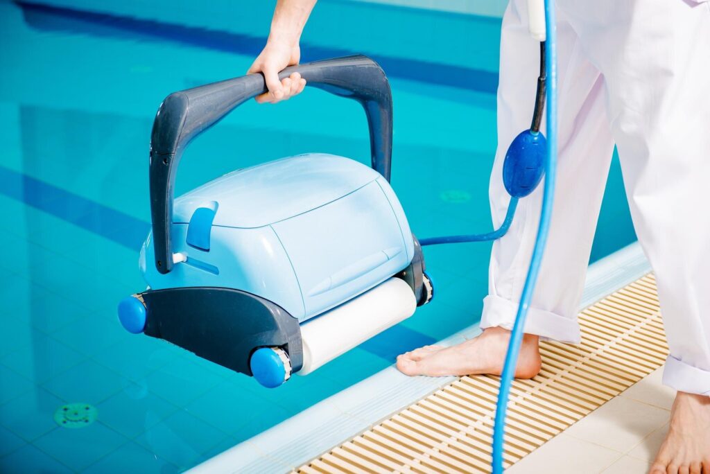 Ein Poolroboter wird an seinem Griff über die Beckenkante gehalten
