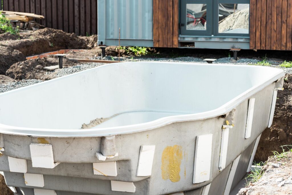 Einteilige GFK-Wanne mit weißer Innenschale in der Baugrube vor einem Haus
