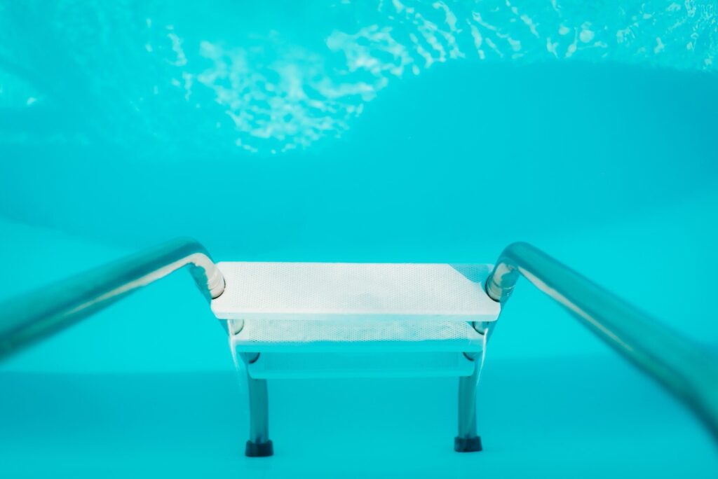 Blick unter Wasser auf die Beckenwand eines Pools mit eingehängter Edelstahlleiter