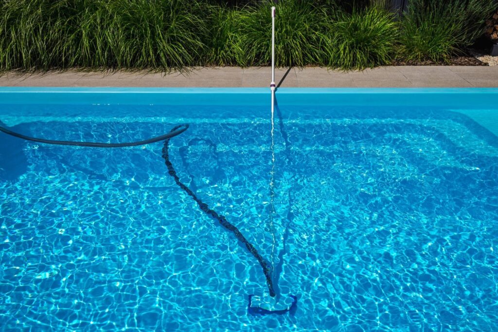 Teleskopstange mit Saugkopf und Schlauch am Boden eines vollen Pools