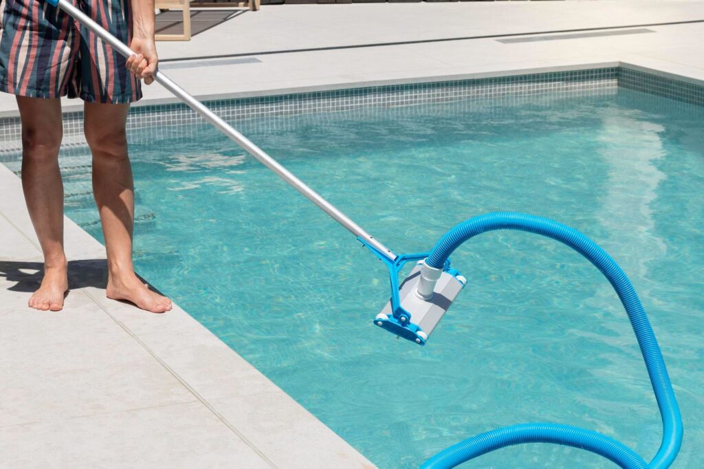 Eine Person reinigt den Pool mit einem Handsauger an Teleskopstange und Schlauch