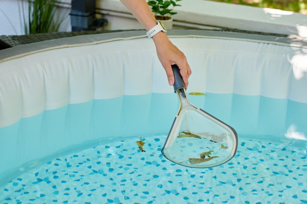 Hand keschert Laub aus einem aufblasbaren Whirlpool